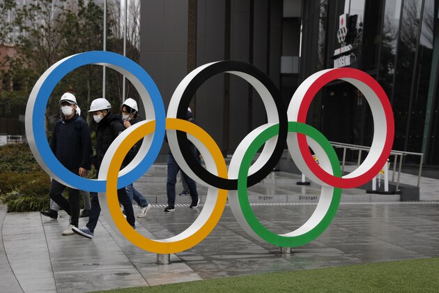 People wearing masks walk past the Olympic rings near the New National Stadium in Tokyo, Wednesday, March 4, 2020. The Tokyo Olympics are being threatened by a fast-spreading virus that has shut down most schools, sports competitions and Olympic-related events in Japan. (AP Photo/Jae C. Hong)