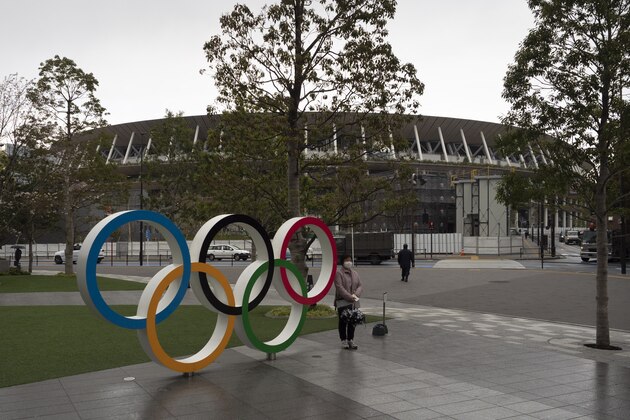A woman pauses for photos next to the Olympic rings near the New National Stadium in Tokyo, Monday, March 23, 2020. The IOC will take up to four weeks to consider postponing the Tokyo Olympics amid mounting criticism of its handling of the coronavirus crisis that now includes a call for delay from the leader of track and field, the biggest sport at the games. (AP Photo/Jae C. Hong)