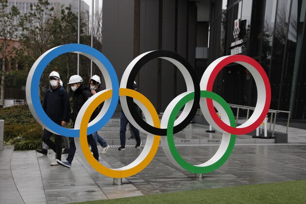 People wearing masks walk past the Olympic rings near the New National Stadium in Tokyo, Wednesday, March 4, 2020. The Tokyo Olympics are being threatened by a fast-spreading virus that has shut down most schools, sports competitions and Olympic-related events in Japan. (AP Photo/Jae C. Hong)