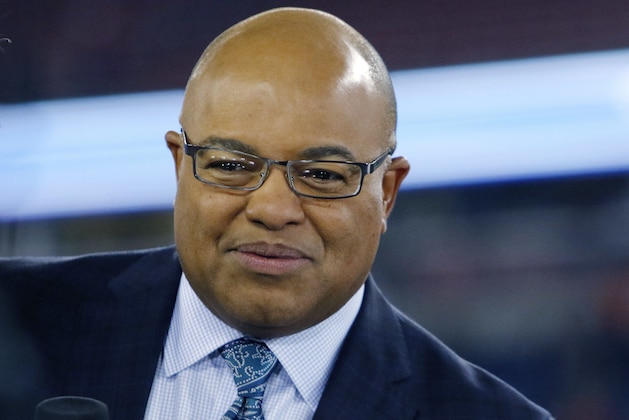 NFL sportscaster Mike Tirico sits on the sideline set before an NFL football game between the New England Patriots and the Atlanta Falcons, Sunday, Oct. 22, 2017, in Foxborough, Mass. (AP Photo/Bill Sikes)