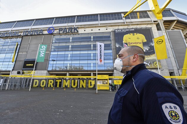 Security with face masks stand in front of the Signal Iduna Park, Germany's biggest stadium of Bundesliga soccer club Borussia Dortmund, where a temporary coronavirus treatment center opened today in Dortmund, Germany, Saturday, April 4, 2020. Instead of the originally scheduled today football clash between Dortmund and Bayern, parts of the stadium were turned into a medical center for outpatient treatment and consultation. The new coronavirus causes mild or moderate symptoms for most people, but for some, especially older adults and people with existing health problems, it can cause more severe illness or death. (AP Photo/Martin Meissner)