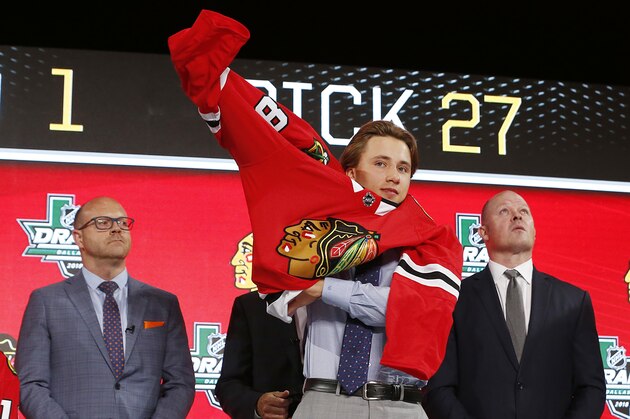 Nicolas Beaudin, of Canada, puts on a jersey after being selected by the Chicago Blackhawks during the NHL hockey draft in Dallas, Friday, June 22, 2018. (AP Photo/Michael Ainsworth)