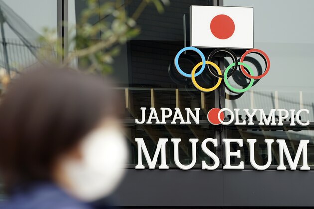 A woman wearing a mask against the spread of the new coronavirus walks in front of the Japan Olympic Museum building in Tokyo Tuesday, April 21, 2020. An open conflict broke out Tuesday between Tokyo Olympic organizers and the IOC over how much to divulge about who will pay for the unprecedented year-long postponement. (AP Photo/Eugene Hoshiko)