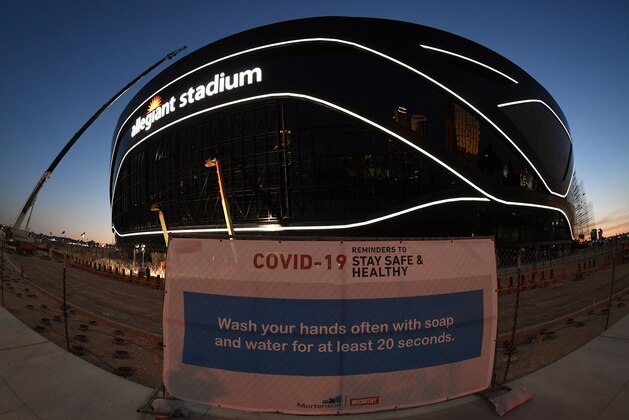 LAS VEGAS, NEVADA - APRIL 23:  (EDITORS NOTE: This image was shot with a fisheye lens.) A sign with guidelines for how to stay safe from the coronavirus is posted on a fence while crews test out architectural light ribbons and exterior sign lighting as construction continues at Allegiant Stadium, the USD 2 billion, glass-domed future home of the Las Vegas Raiders on April 23, 2020 in Las Vegas, Nevada. The Raiders and the UNLV Rebels football teams are scheduled to begin play at the 65,000-seat facility in their 2020 seasons. The World Health Organization declared the coronavirus (COVID-19) a pandemic on March 11th.  (Photo by Ethan Miller/Getty Images)
