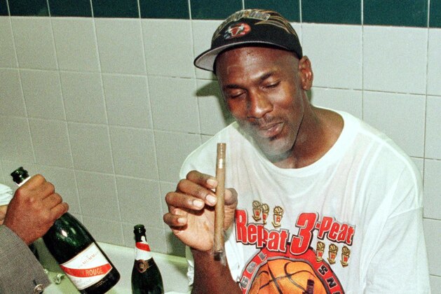 SALT LAKE CITY, UNITED STATES:  Michael Jordan of the Chicago Bulls enjoys a cigar in the locker room 14 June after winning game six of the NBA Finals against the Utah Jazz at the Delta Center in Salt Lake City, UT. The Bulls won the game 87-86 to win their sixth NBA Championship.  AFP PHOTO/MIKE NELSON (Photo credit should read MIKE NELSON/AFP via Getty Images)