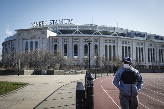 A pedestrian walks a running track while wearing a surgical mask near Yankee Stadium as it remains closed due to COVID-19 concerns, Thursday, March 26, 2020, in the Bronx borough of New York. To baseball fans, opening day is an annual rite of spring that evokes great anticipation and warm memories. This year's season was scheduled to begin Thursday, but there will be no games for a while because of the coronavirus outbreak. Major League Baseball has postponed opening day until mid-May at the earliest. (AP Photo/John Minchillo)
