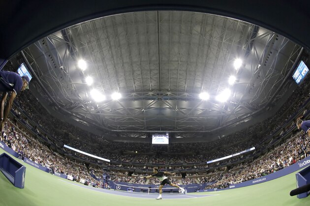 Roger Federer, center, of Switzerland, returns a shot to Frances Tiafoe, of the United States, under the closed roof at Arthur Ashe Stadium during the U.S. Open tennis tournament, Tuesday, Aug. 29, 2017, in New York. Play was suspended on the outer courts because of rain. (AP Photo/Julio Cortez)