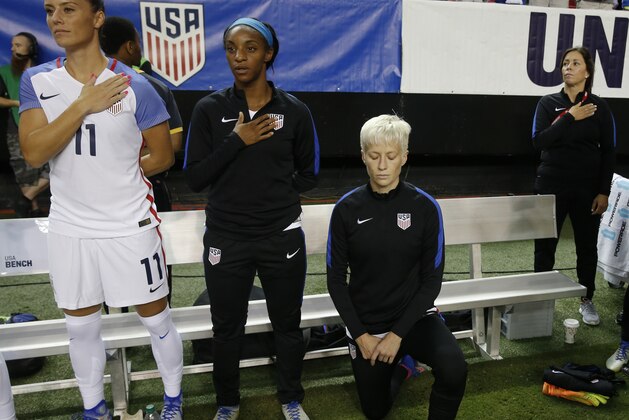FILE - In this Sunday, Sept. 18, 2016 file photo, United States' Megan Rapinoe, right, kneels next to teammates Ali Krieger (11) and Crystal Dunn (16) as the U.S. national anthem is played before an exhibition soccer match against Netherlands in Atlanta. Megan Rapinoe says she will respect a new U.S. Soccer Federation policy that says national team players