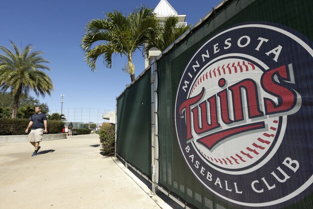 A passerby walks near a Minnesota Twins logo affixed to a fence during spring training baseball practice on Sunday, Feb. 16, 2014, in Fort Myers, Fla. (AP Photo/Steven Senne)
