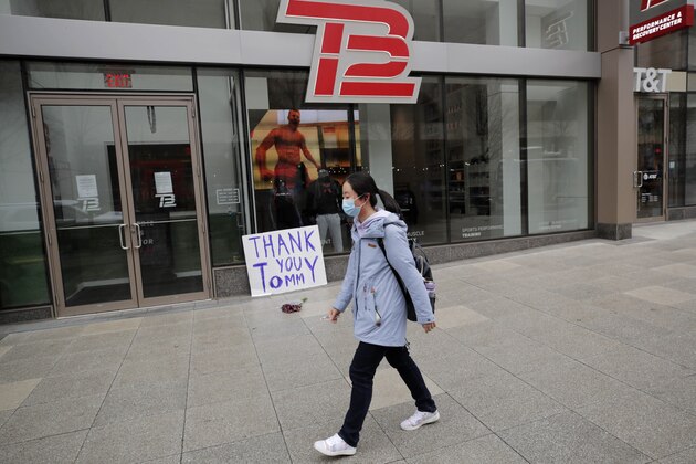 A woman wearing a protective mask walks past a sign thanking former New England Patriots quarterback Tom Brady, who announced he was leaving the football team, outside the TB12 training center in Boston, Tuesday, March 17, 2020. (AP Photo/Charles Krupa)