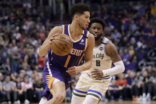 Phoenix Suns guard Devin Booker (1) drives as Milwaukee Bucks guard Wesley Matthews defends during the first half of an NBA basketball game Sunday, March 8, 2020, in Phoenix. (AP Photo/Matt York)