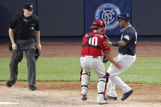 A home plate umpire, left, watches as Philadelphia Phillies catcher J.T. Realmuto (10) tags out New York Yankees Aaron Hicks at the plate during the seventh inning of a baseball game, Monday, July 20, 2020, at Yankee Stadium in New York. (AP Photo/Kathy Willens)