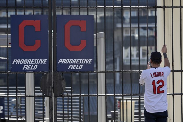 FILE - In this March 26, 2020, file photo, Daniel Clemens looks into the empty ballpark at Progressive Field in Cleveland. Clemens, a season ticket holder, had tickets for the opening day baseball game between the Cleveland Indians and the Detroit Tigers. With no games being played, recent sports headlines have centered around hopes and dreams â€” namely, the uncharted path leagues and teams must navigate to return to competition in the wake of the pandemic. (AP Photo/Tony Dejak, File)