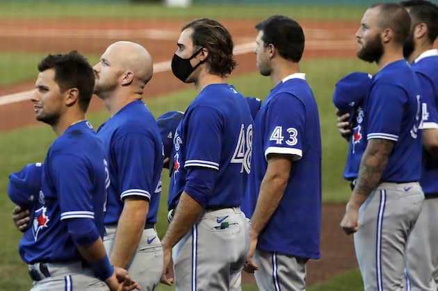 Toronto Blue Jays pitcher Brian Moran, center, wears a protective mask while lined up with teammates during the national anthem prior to an exhibition baseball game against the Boston Red Sox, Tuesday, July 21, 2020, at Fenway Park in Boston. (AP Photo/Charles Krupa)