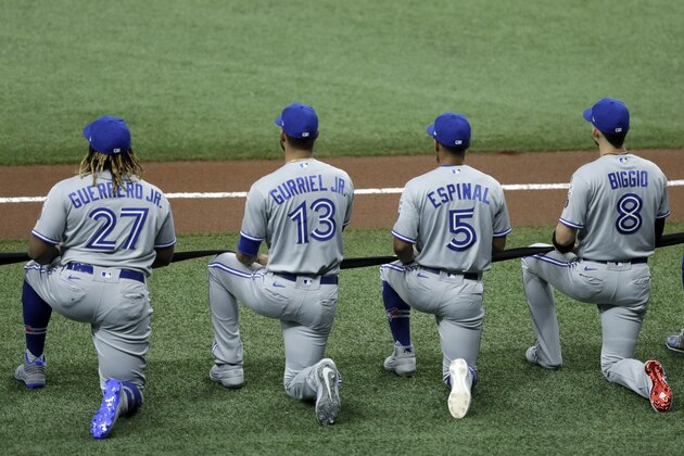 Toronto Blue Jays' Vladimir Guerrero Jr. (27) is joined by teammates Lourdes Gurriel Jr. (13), Santiago Espinal (5), and Cavan Biggio (8) as they hold a black ribbon during the playing of a Black Lives Matter video before a baseball game against the Tampa Bay Rays Friday, July 24, 2020, in St. Petersburg, Fla. (AP Photo/Chris O'Meara)