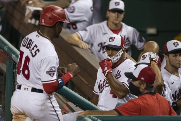 Washington Nationals' Victor Robles (16) comes to the dugout to celebrate scoring as manager Dave Martinez pulls down his mask, during the seventh inning of an exhibition baseball game against the Baltimore Orioles at Nationals Park, Tuesday, July 21, 2020, in Washington. The game was halted due to weather in the eighth inning, with the Nationals leading 6-4. (AP Photo/Alex Brandon)