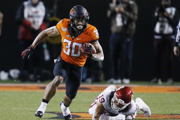 FILE - In this Nov. 30, 2019, file photo, Oklahoma State running back Chuba Hubbard (30) carries past Oklahoma linebacker Caleb Kelly during an NCAA college football game in Stillwater, Okla. Hubbard said on Twitter that he wonâ€™t do anything with the program until there is change after coach Mike Gundy was photographed wearing a T-shirt representing far-right online publication One America News Network. Gundy is seen in a photograph on Twitter wearing the T-shirt with the letters OAN. (AP Photo/Sue Ogrocki, File)