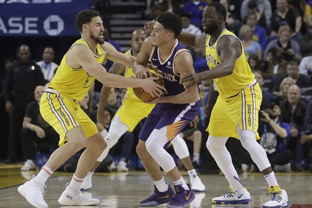 Phoenix Suns guard Devin Booker, center, is defended by Golden State Warriors guard Klay Thompson, left, and forward Draymond Green during the second half of an NBA basketball game in Oakland, Calif., Sunday, March 10, 2019. (AP Photo/Jeff Chiu)