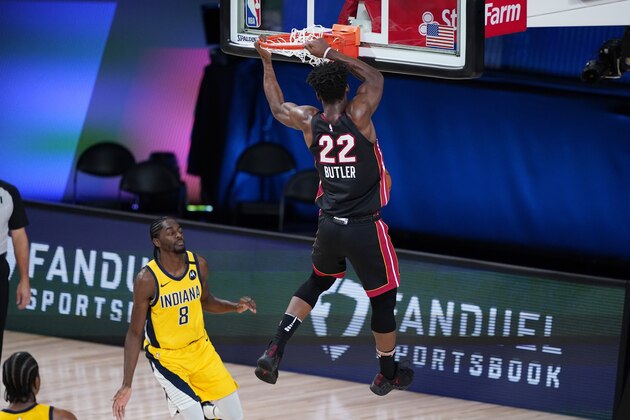 Miami Heat forward Jimmy Butler (22) hangs on the rim after scoring past Indiana Pacers forward Justin Holiday (8) during the first half of an NBA basketball first round playoff game, Tuesday, Aug. 18, 2020, in Lake Buena Vista, Fla. (AP Photo/Ashley Landis, Pool)