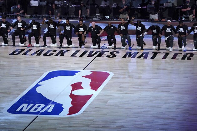 Members of the Orlando Magic and Brooklyn Nets kneel around a Black Lives Matter logo during the national anthem before the start of an NBA basketball game Friday, July 31, 2020, in Lake Buena Vista, Fla. (AP Photo/Ashley Landis, Pool)