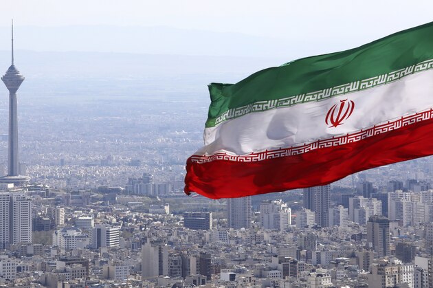 Iran's national flag waves as Milad telecommunications tower and buildings are seen in Tehran, Iran, Tuesday, March 31, 2020. In recent days, Iran which is battling the worst new coronavirus outbreak in the region, has ordered the closure of nonessential businesses and banned intercity travels aimed at preventing the virus' spread.   (AP Photo/Vahid Salemi)