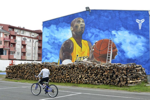 A boy rides a bicycle in front of a new tribute mural honoring former Los Angeles Lakers star Kobe Bryant who was killed in a helicopter crash on Jan. 26, on the school building in Bosanska Gradiska, Bosnia, Wednesday, June 3, 2020. (AP Photo/Radivoje Pavicic)