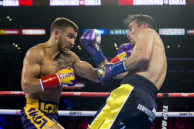 FILE - In this April 12, 2019, file photo, Vasiliy Lomachenko, left, from Ukraine, hits Anthony Crolla, from Britain, during a WBA and WBO lightweight title boxing match in Los Angeles. In ordinary times Vasiliy Lomachenko and Teofimo Lopez would be the fight of the fall, a lightweight title match about as compelling as it gets in the boxing world these days. Instead of a big crowd, the only fans at the MGM Grand conference center will be a few hundred sponsors and first responders with special invites. And, instead of pay-per-view, the fight will be televised live on ESPN, guaranteeing a larger audience than a pay-per-view even if the money isnâ€™t nearly the same. (AP Photo/Damian Dovarganes, File)