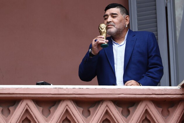 Former soccer great Diego Maradona holds up a small, generic replica of a FIFA World Cup soccer trophy as he kisses it in front of fans below at the Casa Rosada government house after his meeting with Argentine President Alberto Fernandez in Buenos Aires, Argentina, Thursday, Dec. 26, 2019. Decades ago, Maradona held up his team's real trophy at this spot on the balcony after winning the World Cup in Mexico in 1986.  (AP Photo/Marcos Brindicci)