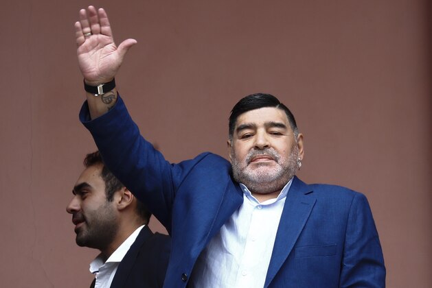 Former soccer great Diego Maradona waves to fans next to a small, generic replica of a FIFA World Cup soccer trophy at the Casa Rosada government house after his meeting with Argentine President Alberto Fernandez in Buenos Aires, Argentina, Thursday, Dec. 26, 2019. Decades ago, Maradona held up his team's real trophy at this spot on the balcony after winning the World Cup in Mexico in 1986.  (AP Photo/Marcos Brindicci)