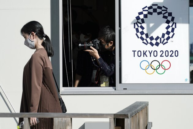 A staff member wearing a face mask walks past the logo of Tokyo 2020 Olympics during a screening test for spectators and officials to ensure a safe and secure the Games Wednesday, Oct. 21, 2020, in Tokyo. Tokyo Olympic officials say they don't know exactly what measures will be taken against the COVID-19 pandemic at next year's Games, but they want the world to know they're working on it. (AP Photo/Eugene Hoshiko)