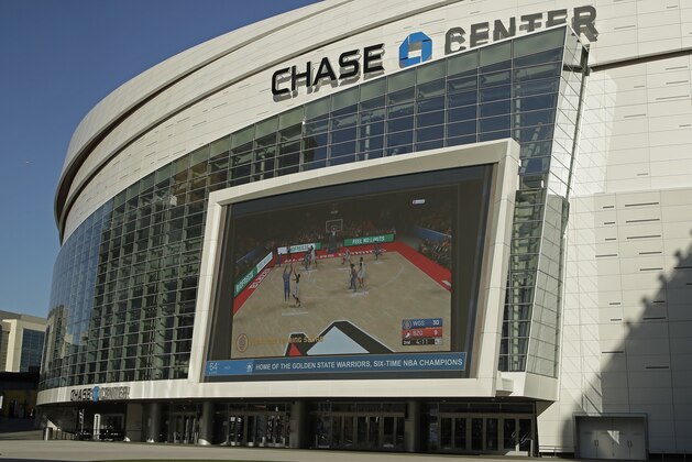 The Chase Center, home of NBA basketball's Golden State Warriors, show a pre-recorded video of a basketball game on a large screen at the entrance to the areana on a day the team was to play the Brooklyn Nets, Thursday, March 12, 2020, in San Francisco. The NBA suspended its season after a Utah Jazz player tested positive Wednesday for the coronavirus. (AP Photo/Ben Margot)