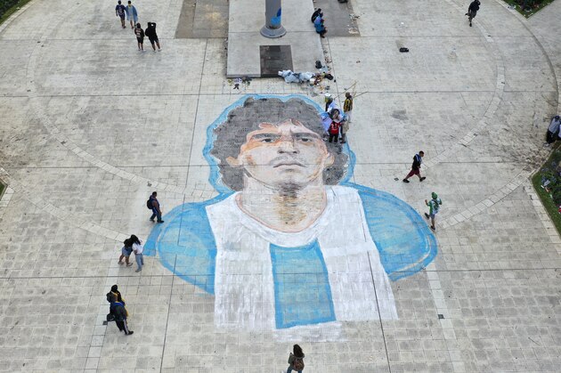 People walk past of the face of Diego Maradona painted on the Plaza de Mayo in front of the presidential palace in Buenos Aires, Argentina, Thursday, Nov. 26, 2020. The Argentine soccer great who led his country to the 1986 World Cup died Wednesday at the age of 60. (AP Photo/Rodrigo Abd)
