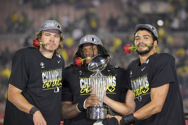 Oregon quarterback Justin Herbert, from left, defensive tackle Jordon Scott and linebacker Troy Dye celebrates with the trophy after their win against Wisconsin in the Rose Bowl NCAA college football game Wednesday, Jan. 1, 2020, in Pasadena, Calif. (AP Photo/Mark J. Terrill)