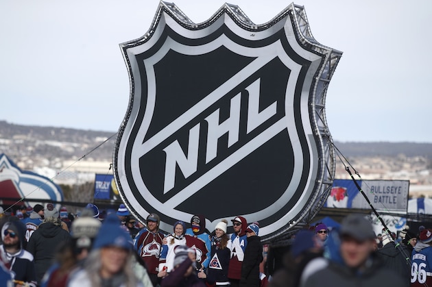 FILE - In this Feb. 15, 2020, file photo, fans pose below the NHL league logo at a display outside Falcon Stadium before an NHL Stadium Series outdoor hockey game between the Los Angeles Kings and Colorado Avalanche, at Air Force Academy, Colo. The uncertainty raised by coronavirus pandemic leads to experts providing a bleak short-term assessment on the NHL's financial bottom line, with some projecting revenues being cut by almost half. What's unclear is how large the impact might be until it can be determined when fans can resume attending games and if the league is able to complete this season. (AP Photo/David Zalubowski, File)
