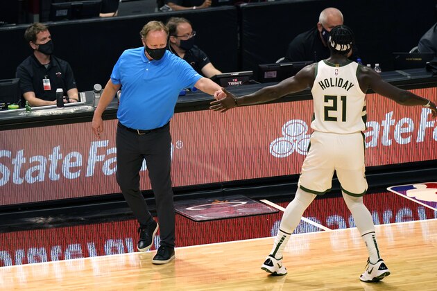 Milwaukee Bucks coach Mike Budenholzer, left, uses his fist to bump the hand of Jrue Holiday (21) during the first half of the team's NBA basketball game against the Miami Heat, Tuesday, Dec. 29, 2020, in Miami. (AP Photo/Lynne Sladky)