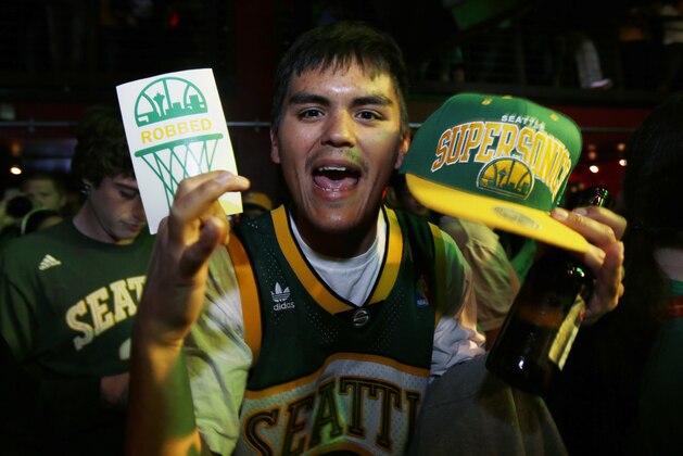 A fan holds a Seattle SuperSonics NBA basketball cap and a sign that reads