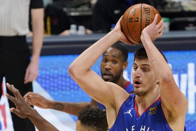 Denver Nuggets center Nikola Jokic, back, looks to pass the ball as Golden State Warriors forward Andrew Wiggins defends in the first half of an NBA basketball game, Thursday, Jan. 14, 2021, in Denver. (AP Photo/David Zalubowski)