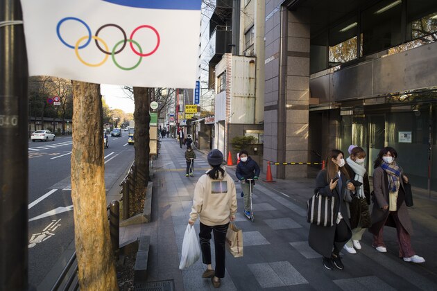 People wearing face masks walk and ride past an Olympics decoration installed along a street in Tokyo on Thursday, Jan. 21, 2021. (AP Photo/Hiro Komae)