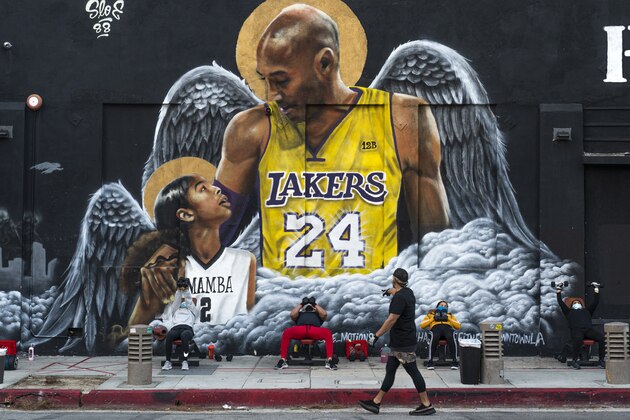 People lift weights on a sidewalk outside the Hardcore Fitness gym, due to COVID-19 restrictions, under a mural honoring NBA star Kobe Bryant and his daughter Gigi near Staples Center in downtown Los Angeles, Monday, Jan. 25, 2021. Bryant, who became one of the greatest basketball players of his generation during a 20-year career with the Lakers, died in a helicopter crash with his daughter Gigi and other passengers on Sunday, Jan. 26, 2020. (AP Photo/Damian Dovarganes)