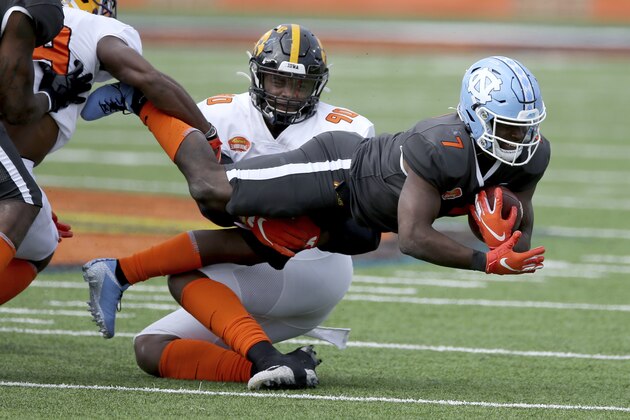 National Team running back Michael Carter of North Carolina (7) is tackled by American Team linebacker Jabril Cox of LSU (19) and American Team defensive lineman Chauncey Golston of Iowa (90) during the NCAA college football Senior Bowl in Mobile, Ala, Saturday, Jan. 30, 2021. (AP Photo/Rusty Costanza)
