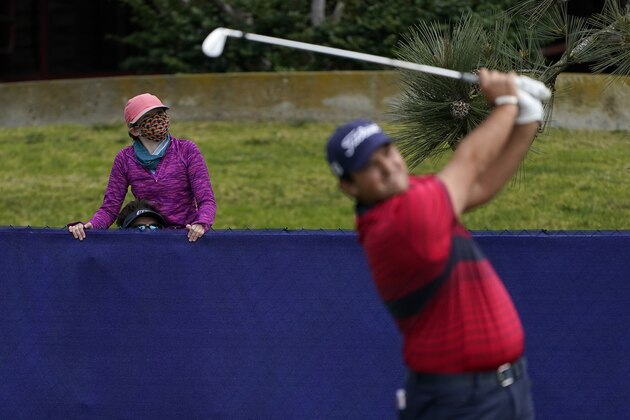 A child wearing a face mask sits on the shoulders of an adult as they watch from behind a fence as Patrick Reed hits from the 11th tee on the South Course during the final round of the Farmers Insurance Open golf tournament at Torrey Pines, Sunday, Jan. 31, 2021, in San Diego. (AP Photo/Gregory Bull)