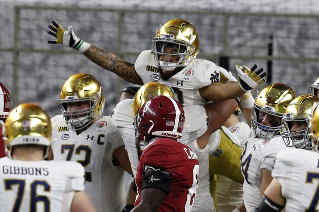 Notre Dame running back Kyren Williams, top, is lifted by offensive lineman Landon Dickerson (69) after Williams' touchdown run as Alabama linebacker Christian Harris (8) looks on in the first half of the Rose Bowl NCAA college football game in Arlington, Texas, Friday, Jan. 1, 2021. (AP Photo/Roger Steinman)