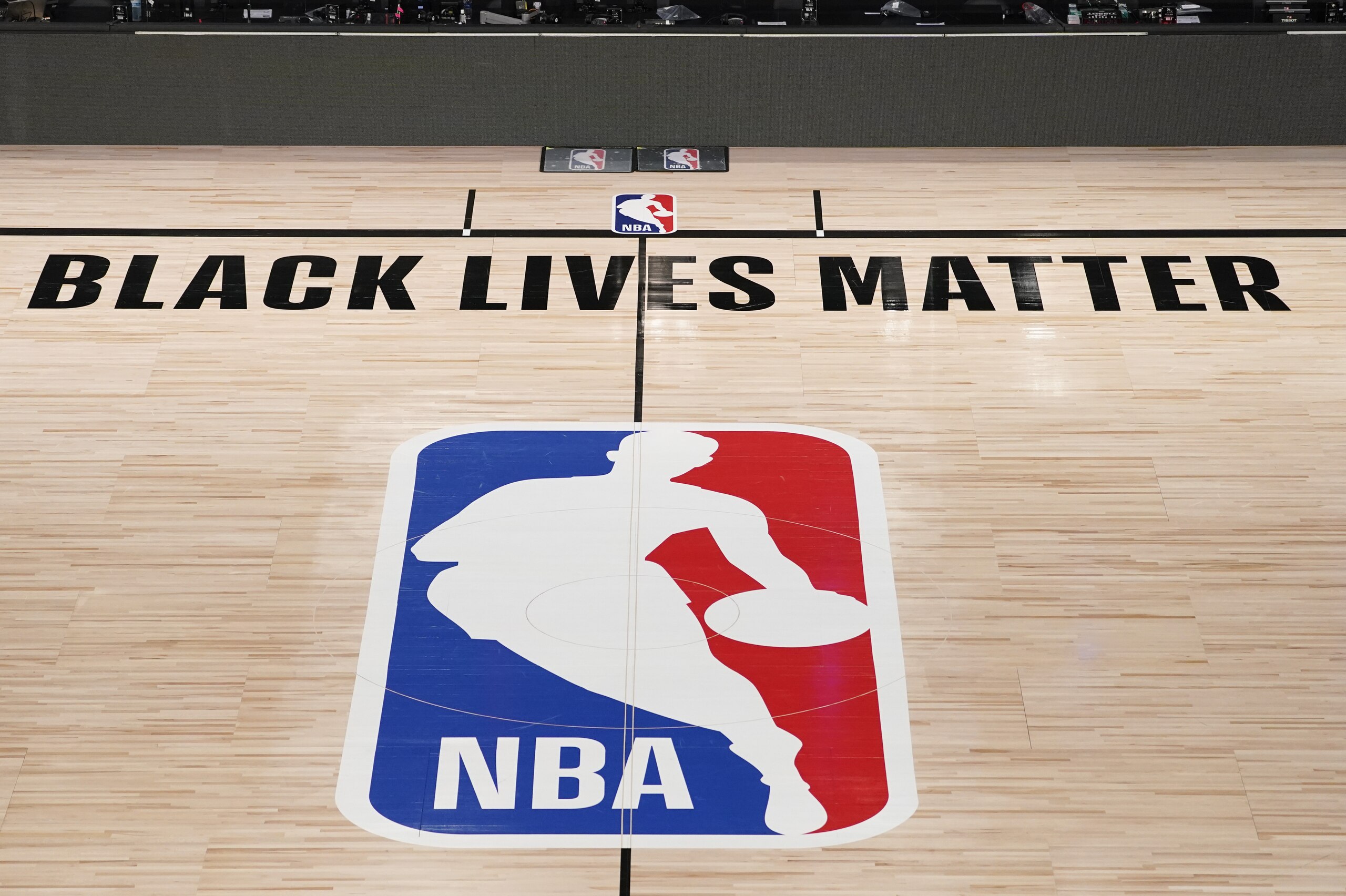 FILE- In this Aug. 28, 2020, file photo, Black Lives Matter is displayed near the NBA logo in an empty basketball arena in Lake Buena Vista, Fla. NBA training camps open around the league Tuesday, Dec. 1, 2020, though on-court sessions will be limited to individual workouts and only for those players who have gotten three negative coronavirus test results back in the last few days.   (AP Photo/Ashley Landis, Pool, File)