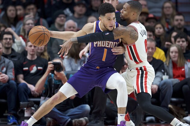 Phoenix Suns guard Devin Booker, left, posts up against Portland Trail Blazers guard Damian Lillard during the first half of an NBA basketball game in Portland, Ore., Monday, Dec. 30, 2019. (AP Photo/Craig Mitchelldyer)