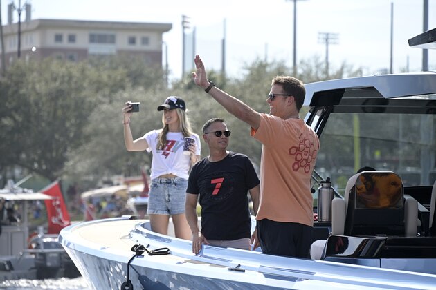 Tampa Bay Buccaneers quarterback Tom Brady waves to fans as his personal trainer Alex Guerrero, left, watches during a celebration of their Super Bowl 55 victory over the Kansas City Chiefs with a boat parade, Wednesday, Feb. 10, 2021, in Tampa, Fla. (AP Photo/Phelan M. Ebenhack)