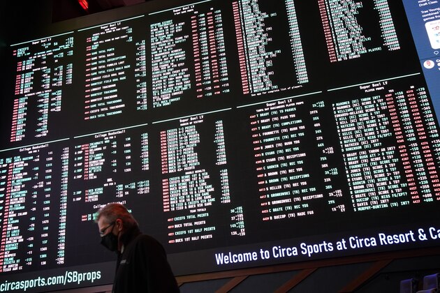 A man walks by as betting odds for NFL football's Super Bowl 55 are displayed on monitors at the Circa resort and casino sports book, Wednesday, Feb. 3, 2021, in Las Vegas. (AP Photo/John Locher)