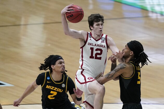 Oklahoma guard Austin Reaves (12) drives to the basket between Missouri guard Drew Buggs (2) and forward Mitchell Smith, right, during the first half of a first-round game in the NCAA men's college basketball tournament at Lucas Oil Stadium, Saturday, March 20, 2021, in Indianapolis. (AP Photo/Darron Cummings)