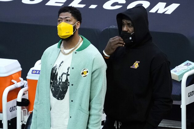 Los Angeles Lakers forward Anthony Davis, left, and forward LeBron James watch from the sideline during the first half of an NBA basketball game against the Phoenix Suns, Sunday, March 21, 2021, in Phoenix. (AP Photo/Rick Scuteri)