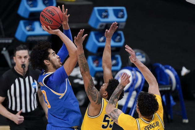 UCLA guard Johnny Juzang, left, shoots over Michigan guard Eli Brooks (55) and forward Brandon Johns Jr., right, during the second half of an Elite 8 game in the NCAA men's college basketball tournament at Lucas Oil Stadium, Tuesday, March 30, 2021, in Indianapolis. (AP Photo/Michael Conroy)