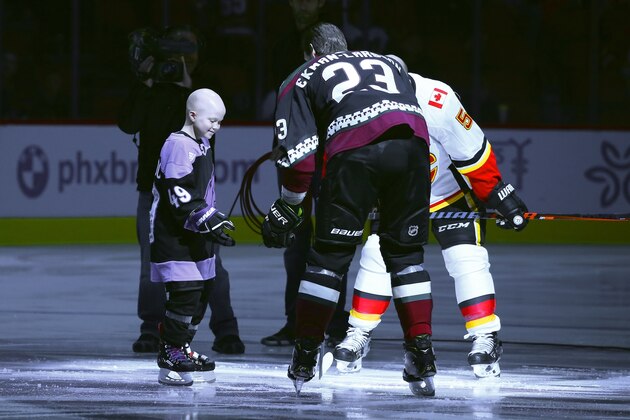 Leighton Accardo, left, who is battling cancer, drops the puck in front of Arizona Coyotes' Oliver Ekman-Larsson (23) and Calgary Flames' Mark Giordano (5) during an NHL Fights Cancer puck drop ceremony prior to an NHL hockey game in Glendale, Ariz., in this Saturday, Nov. 16, 2019, photo. Accardo's will to attack anything in her path, even terminal cancer, lifted an entire organization. The Arizona Coyotes will carry her spirit on by making her the first non-player, general manager or broadcaster to be inducted into an NHL team's ring of honor.  (AP Photo/Ross D. Franklin)